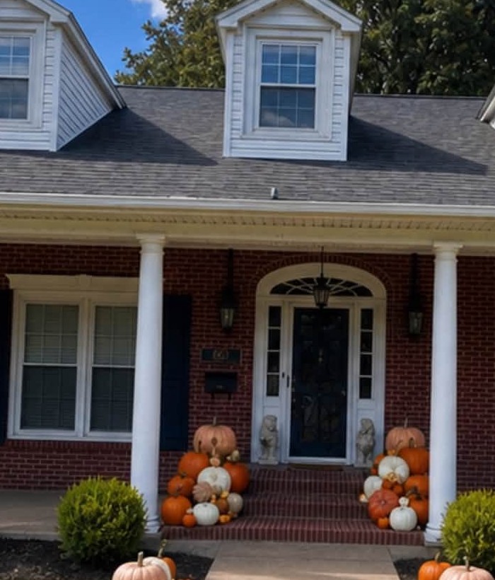 Abundant layered pumpkin display on hay bales flanking a front entrance